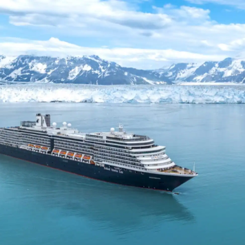 A Holland America Line Cruise Ship sailing in Alaska waters with snow covered mountains in the background