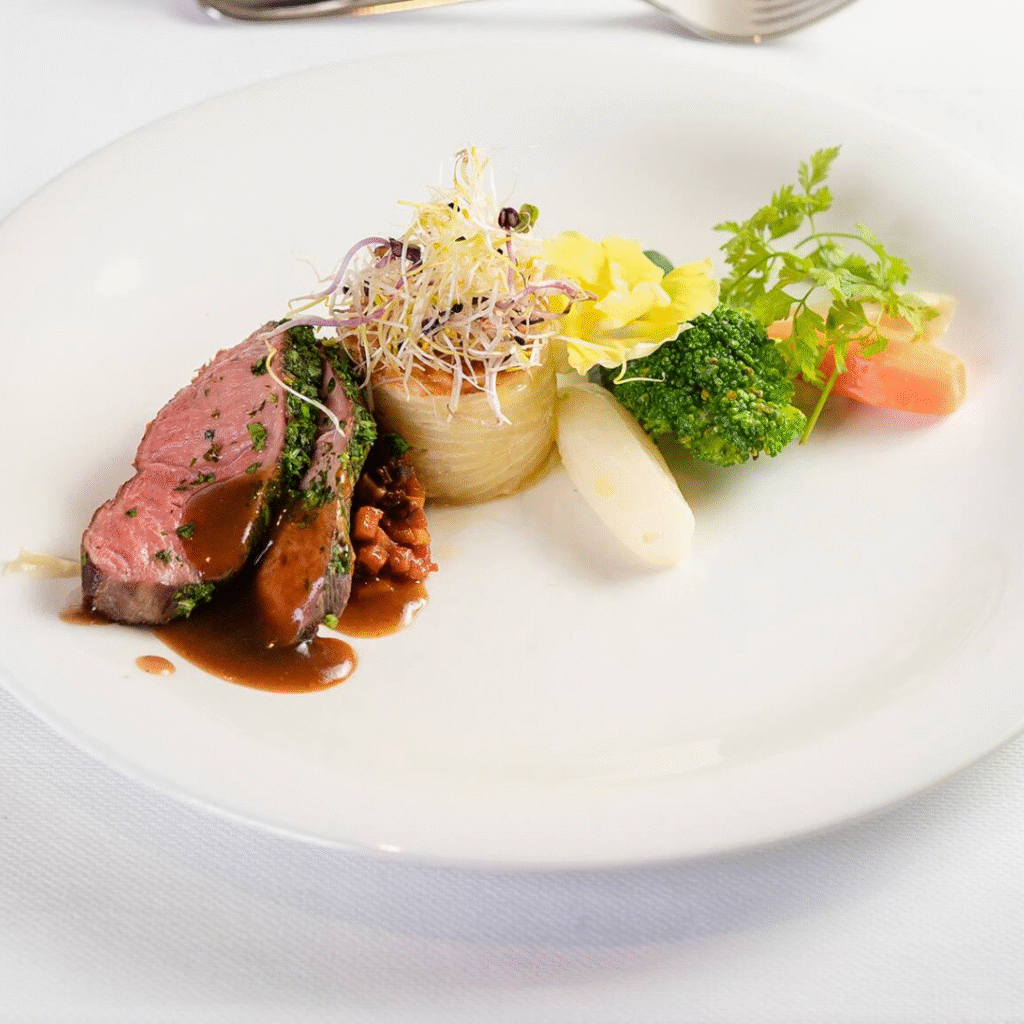 a dinner plate with steak a carrot broccoli and onions covered in a sauce with parsley on top